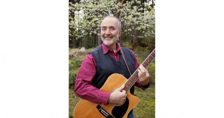 Raffi Cavoukian smiles out at the camera, holding his acoustic guitar.